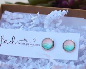 Small silver round stud earrings featuring turquoise blue waves and peach colored sand. On white earring card with Fresh Air Designs Photo.