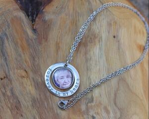 Silver photo charm necklace encircled by a Forever in My Heart charm in a stamped font shown on a natural wood background.