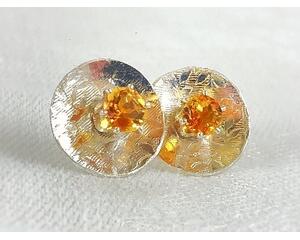 Prong-set golden citrine stud earrings with sterling silver disc jackets. The jackets are embossed with a floral pattern.