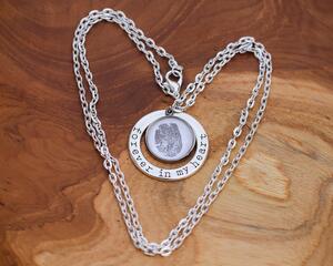 Silver fingerprint charm necklace encircled by forever in my heart accent charm on natural wood background.