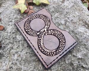 handmade wallet featuring the Ouroboros symbol in natural tan against an antique black leather background with black stitching