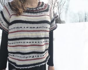 Women's Nursing Access Oversized Cropped Sweater with flutter sleeves that cover the shoulders. Hem extends to the waistline. Features copper, black, and cream yarn on an off white background knit in a garter stitch and criscross stitch stripe pattern. One Size Fits All.