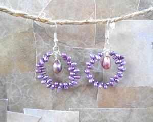 silver hoop earrings with tiny light purple pearls going around the hoop. the hoop is attached to silver earring hooks.