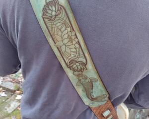 Japanese Koi and lotus flowers are featured on this intricately detailed handmade leather guitar strap with adjustable sizing for custom position height.

The base color of the main section of this strap is hand dyed in Moonlight Blue, which includes muted turquoise and tan tones.  The fish, water lillies, water and scale designs are permanently etched into the leather. The slot pieces are hand dyed in Antique Brown, with the adjustment pieces in Moonlight Blue