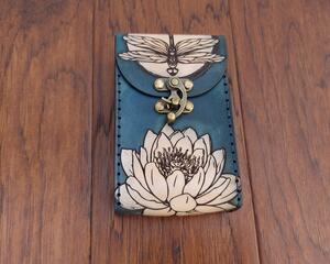 This Premium Handmade Leather Tarot Card Case features a dragonfly over moonlit water lilies. This is a unique 3 color premium leather tarot card box, hand dyed and hand sewn in our shop.

This special and unique find would make a beautiful gift for a tarot enthusiast in your life, or anybody looking to protect their tarot cards, oracle decks, or other small items. 

Featuring artwork permanently etched into the leather in black:

The front of this leather case displays a dragonfly over a full moon which is rising above a water lily.
The back of the case features a moonlit water garden, with water lilies glowing in the moonlight. 
Swirling shades of marbled blue are an interesting backdrop to the art. Our hand-dyed leather process produces an array of shades with incredible depth in the color. The natural character of the real full grain leather combined with the hand dying process makes each case unique.