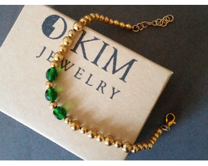 Emerald green and gold beaded bracelet laying on an O Kim Jewelry box.