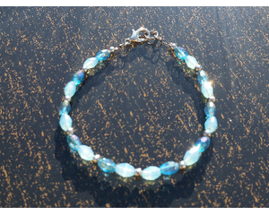 Frozen-theme bracelet rests on a table. There are 3 types of beads: iceberg blue (glass), blizzard blue (glass), & stainless steel (metal).