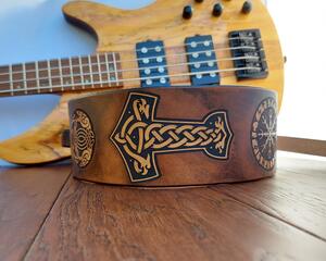 This is a Handmade Leather Guitar Strap Featuring a Viking or Norse motif. Crafted from ultra thick premium vegetable tanned leather, the instrument strap has been hand dyed and tooled, and the details are highlighted in natural tan for eye catching contrast.

Selected portions of the artwork are highlighted in natural tan, with the remainder of the strap hand dyed in a distressed Antique Dark Brown.