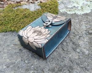 This Premium Handmade Leather Tarot Card Case has been specially sized to accommodate slightly deeper standard sized tarot card decks. The tarot card box features a dragonfly over moonlit water lilies. Featuring artwork permanently etched into the leather in black:
The front of this leather case displays a dragonfly over a full moon which is rising above a water lily.
The back of the case features a moonlit water garden, with water lilies glowing in the moonlight. 
Swirling shades of marbled blue are an interesting backdrop to the art. Our hand-dyed leather process produces an array of shades with incredible depth in the color. The natural character of the real full grain leather combined with the hand dying process makes each case unique.