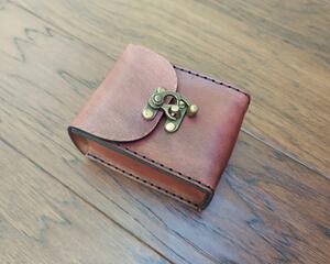 Thick full grained vegetable tanned leather is the star of this hand crafted, high quality playing card case. This case was designed to hold two decks of poker sized playing cards. The leather box has been hand dyed in Antique Mahogany with a weathered look.  Front view of case on table top.