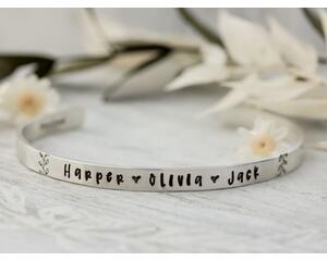 Sterling silver cuff bracelet stamped with kids names and a heart spacer between names with a stamped for detail on both sides. 