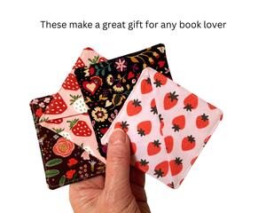 A hand holding 4 different corner bookmarks. Each are made with different fabrics. Two are florals and two are strawberry prints.