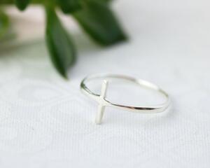 Sleek sterling silver sideways cross ring on white background.
