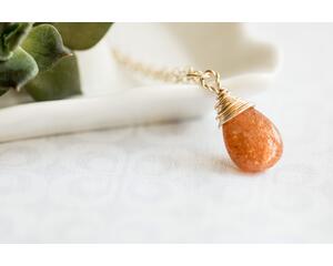 Sunstone necklace, orange briolette in 14K gold, on white dish with green leaves.