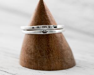  Two sterling silver rings on a wooden cone, one with "SAMI" and paw prints.
