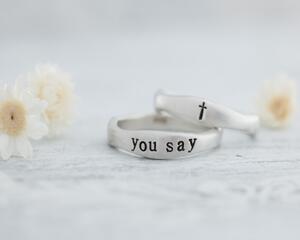 Hand with two sterling silver rings, "YOU SAY" and cross design
