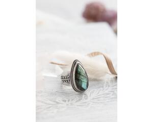 Silver ring with pear-shaped faceted labradorite featuring blue-green opalescent flashes serrated bezel and bead detailing around the bezel.