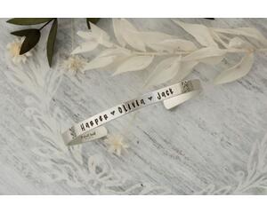 Sterling silver cuff bracelet stamped with kids names in a delicate handwritten font with a stamped for detail on both sides.