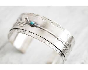 Sterling silver cuff bracelet with embossed arrow overlay accented with a genuine turquoise cabochon. 