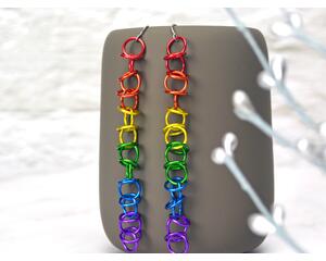 Chainmaille earrings in lgbtq rainbow pride colors hanging from a grey mug. Links are a single strand, with orbital rings.