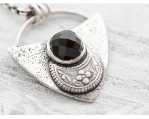 Shield shaped sterling silver pendant with floral patterned moon and faceted black onyx cabochon. 