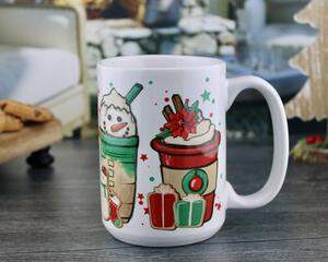 white mug with 4 different Christmas themed  iced coffee cups printed around it. One with candy canes, one with Poinsette, one with a snowman, and one with peppermint candies. Presents, gingerbread man and snowman cookie sit in between the cups.