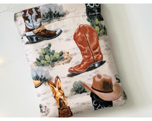 cowboy boots book sleeve has a light rustic brown background, there are cacti and boots, some had cowboy hats on top of them