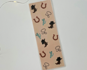 this western bookmark has a brown background with horseshoes, cacti, boots, & rope all over the book mark
