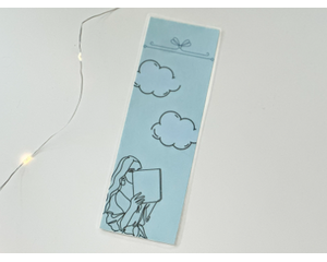 this blue bookmark has a blue background with a girl reading in the bottom left hand corner with clouds in the sky