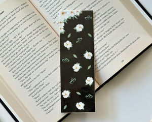this floral bookmark has a black background with white flowers and green leaves and hearts all over the page holder.