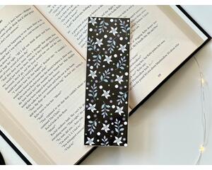 this floral bookmark has a black background. white and purple flowers, purple leaves, and white, green, and purple polka dots