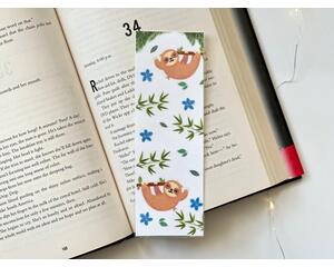 the sloth bookmark has a white background with two sloths hanging from the branches, stems of leaves, blue flowers and leaves all over the bookmark