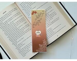 this owl bookmark has an ombre brown background with an owl reading a book in the middle & leaves in the bottom right and top left corner