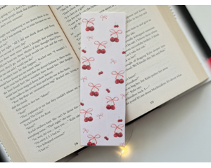 this cherry bookmark has a light pin background with cherries having pink bows on the them, and the smaller ones not having bows on them.