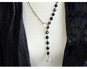 Asymmetrical lariat necklace: one side black coin beads, silver spacers, pewter dangle, other side rhodium chain connected by pewter loop