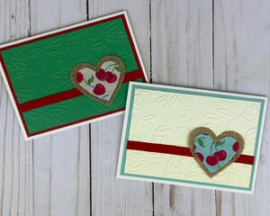 A card making kit with cream and green cherry embossed cardstock, with red ribbons and cherry fabric and burlap heart embellishments.