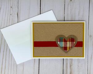 A fall card kit with brown embossed cardstock, yellow cardstock mat, a red ribbon and a plaid fabric and burlap heart embellishment.