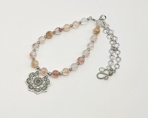 A handcrafted spring-inspired necklace featuring sun hematoid quartz beads, a floral pendant, and a rhodium chain.