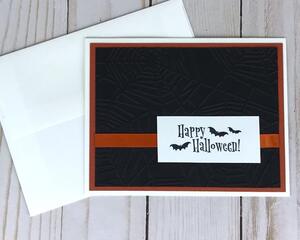 A Halloween card kit with black embossed cardstock, orange cardstock mat, 'Happy Halloween" sentiments and orange ribbons.