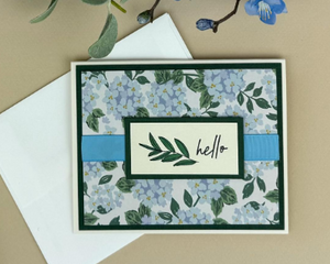 A flower card making kit with green cardstock, hydrangea scrapbook paper. stamped "hello" sentiments, light blue ribbons and cards/envelopes