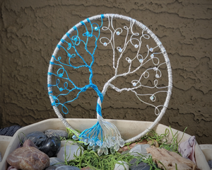 front view blue and white tree made with aluminum wire standing in bed of polished rocks and a dark background.