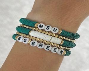 Stack of green and gold beaded stretch bracelets with white letter beads spelling ‘MSU’ and ‘GO GREEN’ on a wrist. Michigan State University