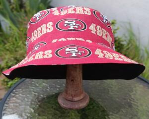 Front view of bucket hat on stand. Fabric has red and gold SF 49ers logos on red background.
