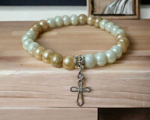 This is a white and beige pear stretch bracelet with a cross charm.