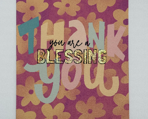 Vertical floral card with thank you written in multi color text with ‘You are a blessing’ written in black text over design. Glitter accents