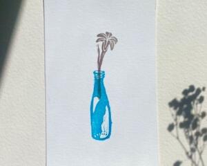 The front of this print features a lovely day lily sprouting out of a blue glass bottle.