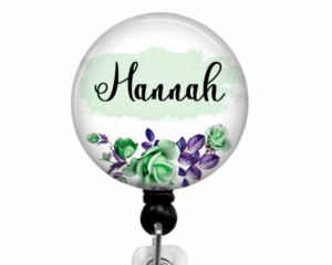 Green and purple flowers with the  name Hannah in black on a light green background affixed to a black retractable badge reel.