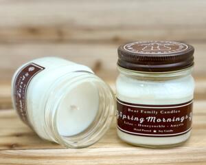 Lilac scented soy candle in 8oz mason jar. One jar standing up with lid on and one jar on its side with lid off.