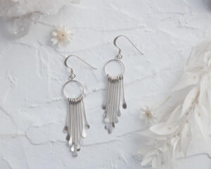  Pair of 925 sterling silver fringe dangle earrings displayed on a textured white surface with flowers and crystals.
