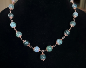Moss agate beads in shades of teal, green and blue are linked by wire wrapping to form a necklace with copper clasp. 